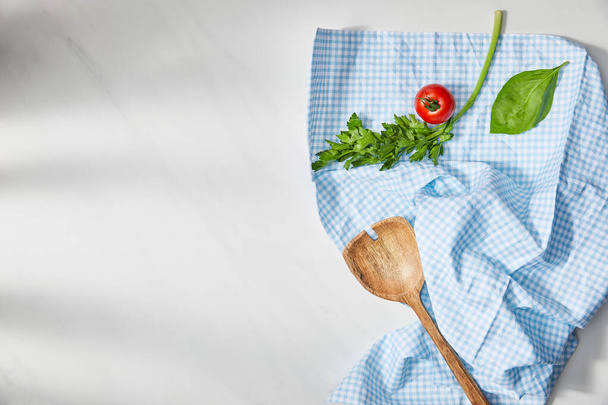 Fesleğen yaprağı, maydanoz, vişneli domates ve beyaz arka planda ekose kumaş üzerine spatula manzarası. - Fotoğraf, Görsel