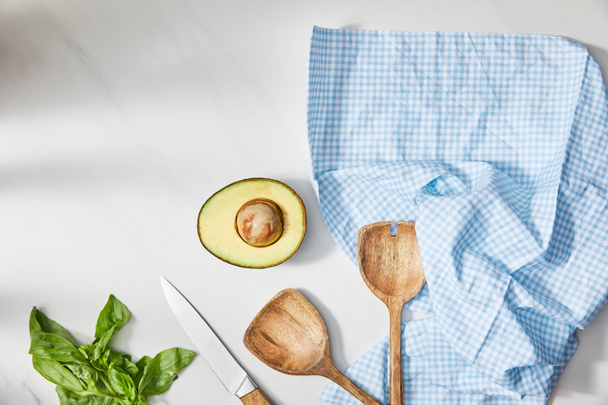 Top view of basil, knife, spatulas and avocado half near plaid cloth on white background - 写真・画像