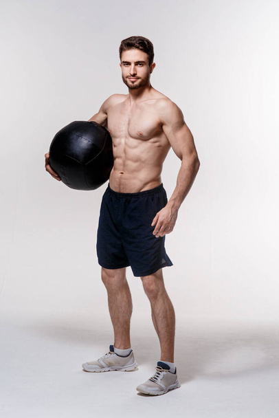 a male athlete in good physical shape on white background with a medball in his hands. - 写真・画像