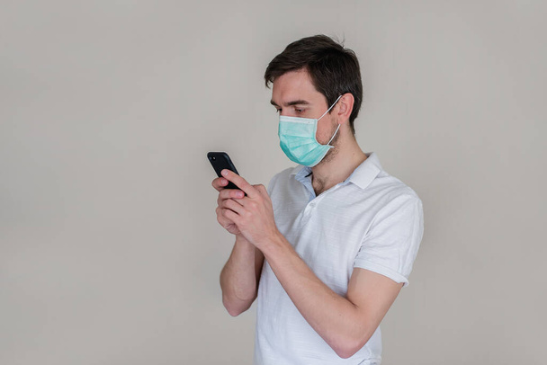 Remote work. The guy in the medical mask is working on a laptop and talking on the phone. A man in a medical mask takes a selfie. - Фото, изображение