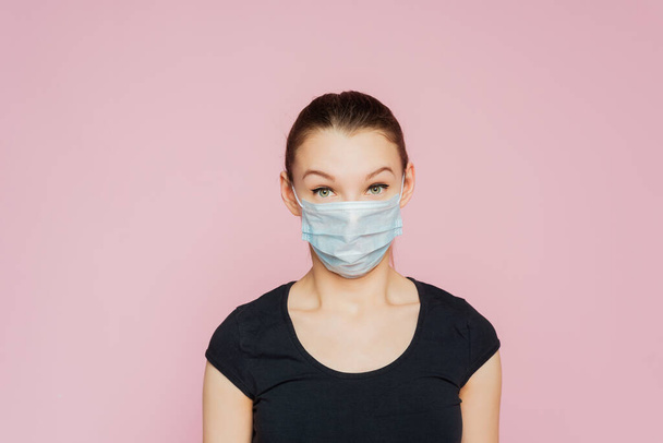 顔の医療用マスクを身に着けている女性のスタジオの肖像画、カメラを見て、ピンクの背景に隔離され、閉じます。インフルエンザの流行、ほこりアレルギー、ウイルスからの保護。Covid-19, coronavirusパンデミック. - 写真・画像