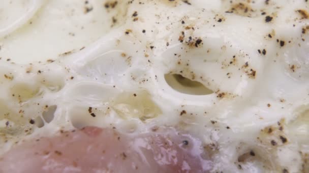 Makro shot z białek jaj smażonych pokryte czarnym pieprzem w patelni - Materiał filmowy, wideo