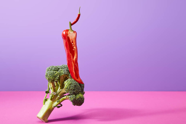 połowa papryki chili na wierzchu dojrzałych brokułów na fioletowo-różowym    - Zdjęcie, obraz