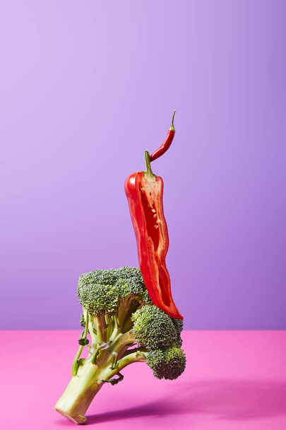 half chili peper bovenop rauwe broccoli op paars en roze   - Foto, afbeelding