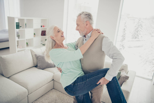 Portrait of cheerful lovely spouses moving laughing in apartment dressed jeans denim trousers teal brown sweater - Φωτογραφία, εικόνα