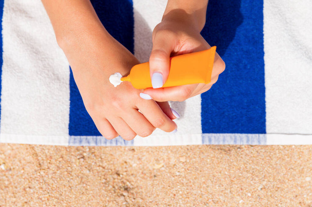 Beautiful lady is sunbathing on the towel on the sand at the beach and protects her hands with sunblock. - Photo, Image