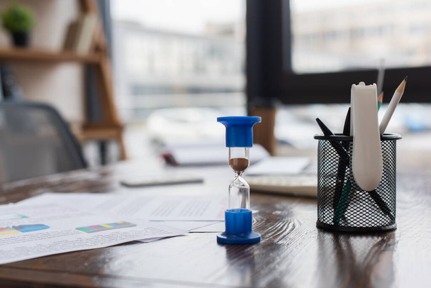 Песочные часы рядом с держателем ручки на столе в офисе
 - Фото, изображение