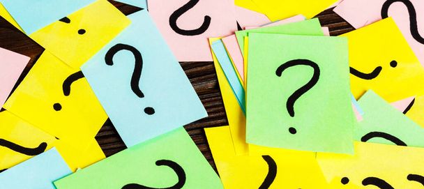 Pile of colorful paper notes with question marks on wooden background. Closeup. - Photo, Image