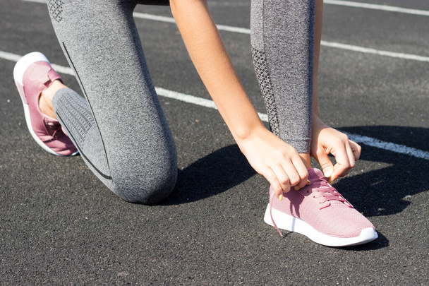 Обрізати зображення підходящої жінки, зав'язуючи шнурки на біговій доріжці на стадіоні. Спортсменка готується до фізичних вправ і бігає
. - Фото, зображення