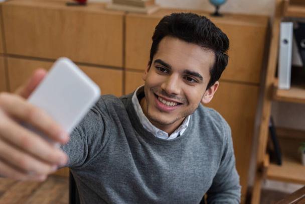Selektywne skupienie biznesmena uśmiechającego się i robiącego selfie w biurze - Zdjęcie, obraz
