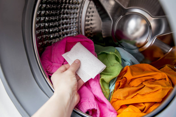 Рука жінки кладе кольоровий поглинаючий лист всередину пральної машини, дозволяє мити змішані кольори одягу без руйнування концепції кольорів
. - Фото, зображення