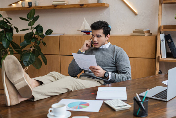 Uomo d'affari con carta mettere le gambe sul tavolo e parlare su smartphone in ufficio
 - Foto, immagini