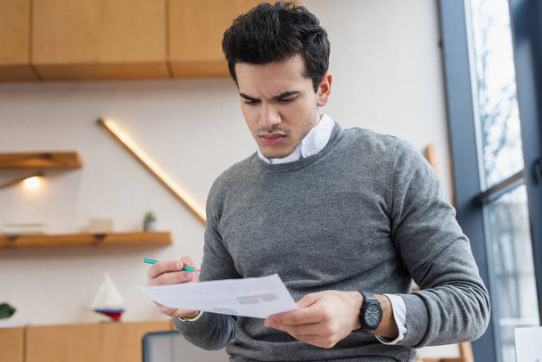 Worried businessman with pencil looking at paper in office - Photo, Image