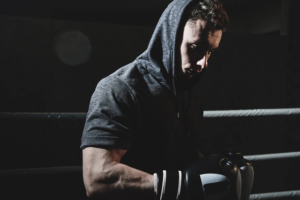 Closeup portrait of a professional boxer in a hood and gloves in the ring. Dark colors, face in shadow - Photo, image