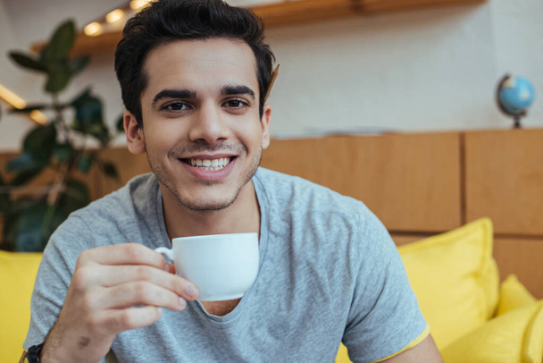 Mann mit Tasse Kaffee lächelt und blickt in Kamera - Foto, Bild