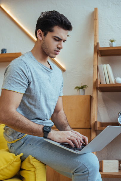 Geconcentreerde freelancer werkt met laptop op de bank in de woonkamer - Foto, afbeelding