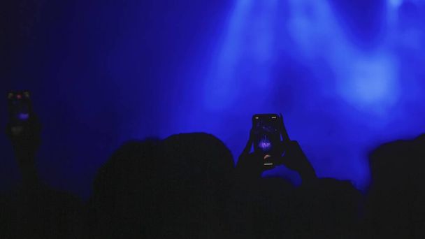 Real live streaming in disco hall during party. Silhouette hands of audience taking photo with mobile phone. Recording Video in party. - 写真・画像