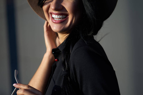 Closeup portrait happy beautiful girl with charming smile and long brunette hair wearing stylish black dress and fashionable hat.                                - Photo, Image