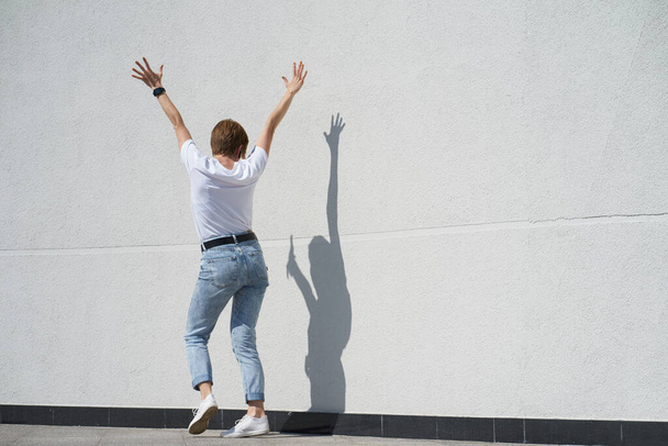 Κοντή κοκκινομάλλα κοπέλα χορεύει με σκιά μπροστά από το λευκό τοίχο outdors το καλοκαίρι  - Φωτογραφία, εικόνα