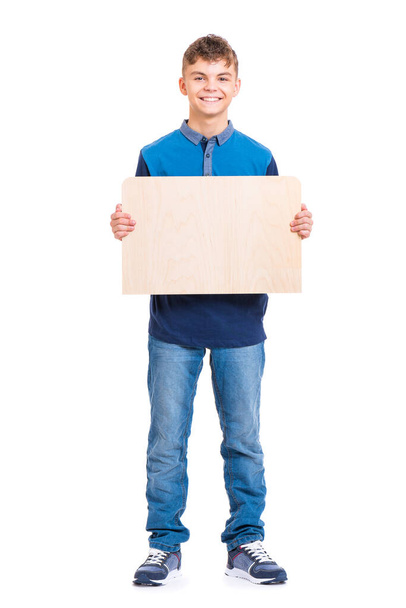 Full length portrait of young caucasian teen boy holding wooden board. Funny teenager showing empty billboard sign and looking at camera, isolated on white background. - Foto, afbeelding