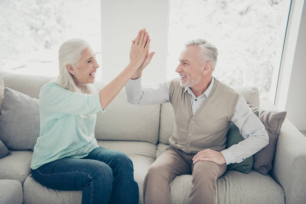 Portrait of lovely grandparents giving high five enjoying wearing teal brown jumpers trousers jeans sitting divan room - Фото, зображення