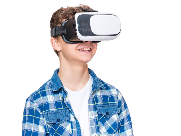 Happy teen boy wearing virtual reality goggles watching movies or playing video games, isolated on white. Cheerful teenager looking in VR glasses. Funny child experiencing 3D gadget technology. - Photo, Image