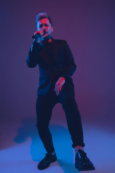 Young caucasian musician, performer singing, dancing in neon light on gradient background - Foto, Imagem