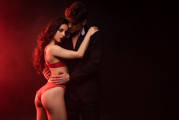 homme en costume câlin sexy copine en lingerie rouge sur noir avec lumière rouge
 - Photo, image