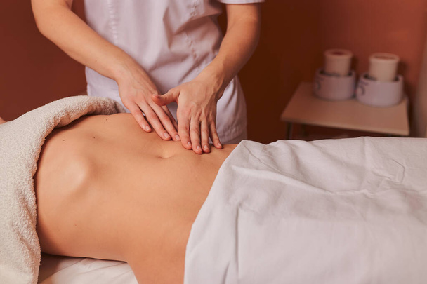 The specialist makes the girl a therapeutic massage of the abdomen on the table in the massage parlor. - Valokuva, kuva