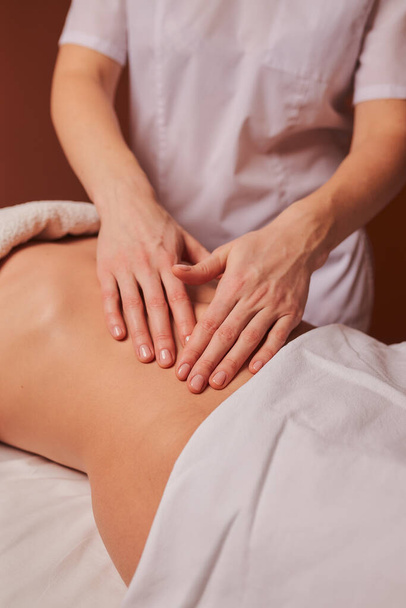 The specialist makes the girl a therapeutic massage of the abdomen on the table in the massage parlor. - Zdjęcie, obraz