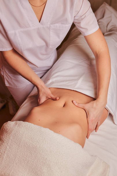 The specialist makes the girl a therapeutic massage of the abdomen on the table in the massage parlor. - Foto, Imagem