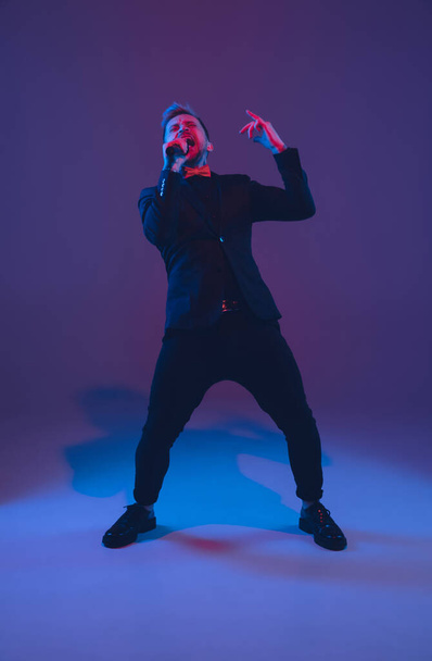 Young caucasian musician, performer singing, dancing in neon light on gradient background - Foto, Bild