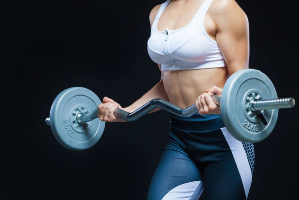 Close-up photo of a fitness Muscular girls hands holding curly barbell at the gym isolated on a black background - Photo, Image