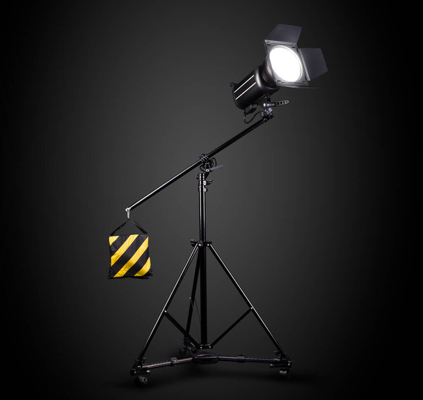 Fotografické studio blesk na osvětlovací stojan izolovaný na černém pozadí s lampou. Profesionální vybavení jako monoblok nebo monolight - Fotografie, Obrázek