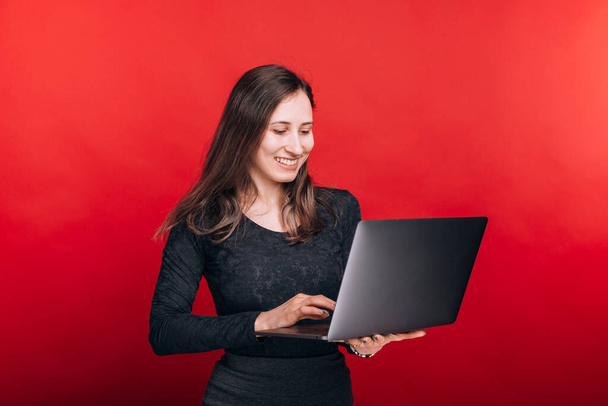 Junge Frau sucht etwas auf ihrem Laptop auf rotem Hintergrund - Foto, Bild