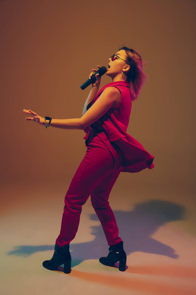 Young caucasian female musician, performer singing, dancing in neon light on gradient background - Φωτογραφία, εικόνα