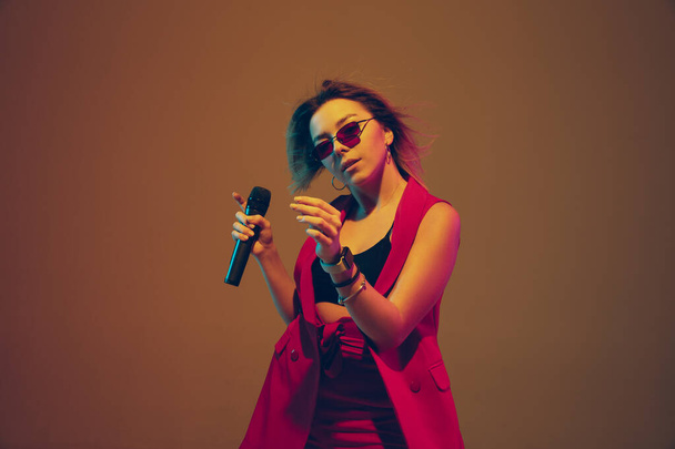 Young caucasian female musician, performer singing, dancing in neon light on gradient background - Foto, Imagem