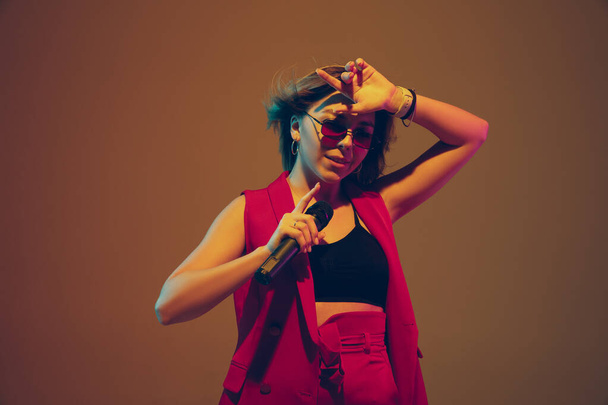 Young caucasian female musician, performer singing, dancing in neon light on gradient background - Fotó, kép