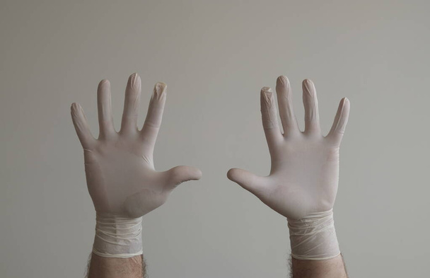 Handen van een man beschermd tegen het coronavirus. Witte latex handschoenen Bescherm uw handpalm tegen infecties, virussen en ziektekiemen. Bescherming van het huidisolatiesymbool tegen het gevaar van infectie. Obstructie, een barrière voor ziekten. - Foto, afbeelding