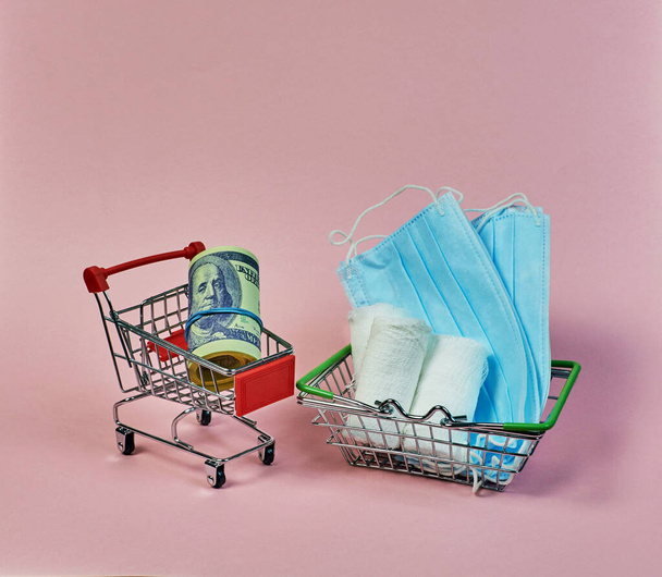 shopping mini trolley with dollars and hygiene masks and bandages on a pink background - Φωτογραφία, εικόνα