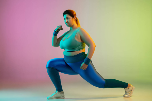 Young caucasian plus size female models training on gradient purple green background - Фото, изображение