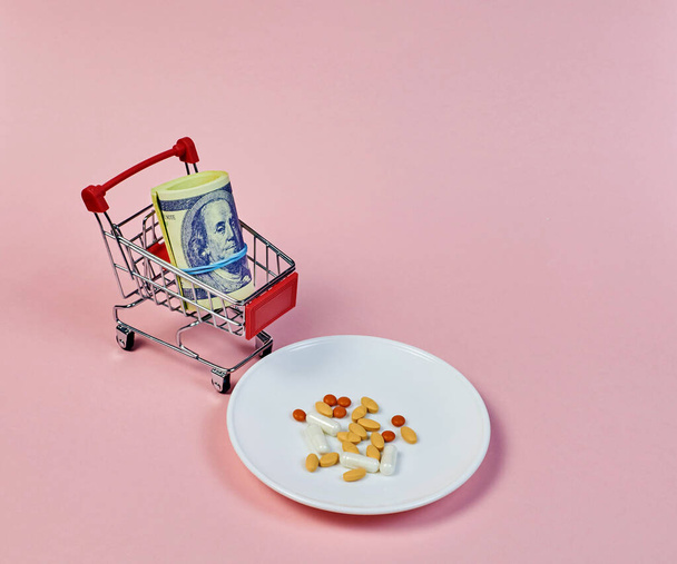 shopping mini trolley with dollars and a plate with different pills - 写真・画像
