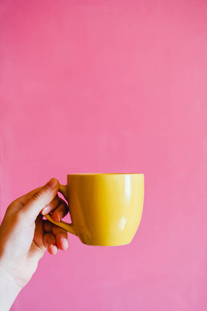 Taza amarilla en la mano con fondo de pared rosa brillante
 - Foto, Imagen