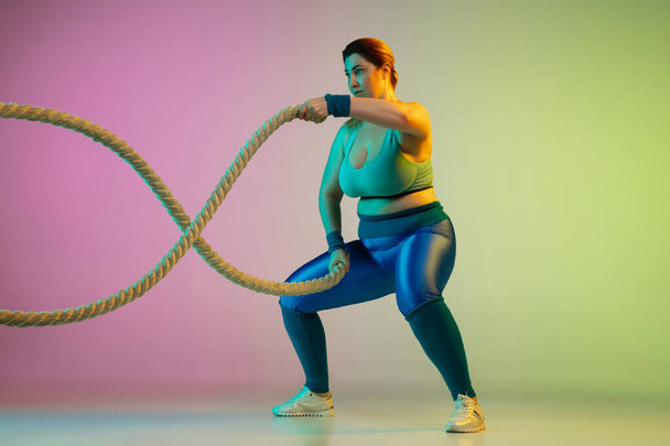 Young caucasian plus size female models training on gradient purple green background - 写真・画像