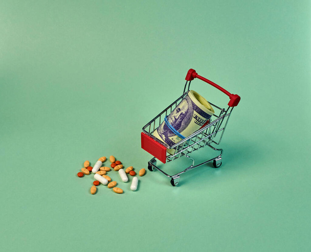 mini shopping trolley with dollars and pills on a gently light green background - Valokuva, kuva