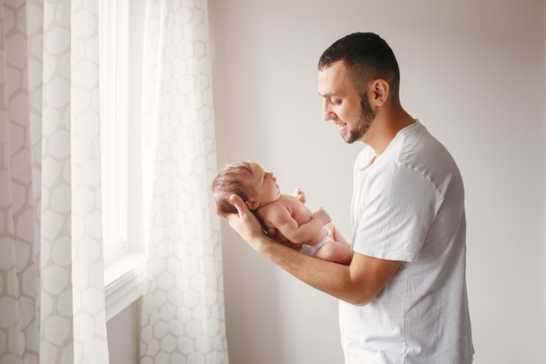 Happy Caucasian father holding newborn baby. Male bearded man parent rocking child daughter son on his hands. Authentic lifestyle candid moment. Young dad family life concept. - Фото, изображение