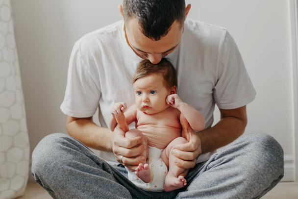 Happy Caucasian father holding newborn baby on laps knees. Man parent embracing rocking child daughter son. Authentic lifestyle candid moment. Proud young dad. Family fathers day - Photo, Image