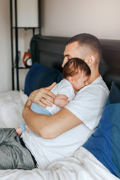 Καυκάσιος πατέρας με νεογέννητο μωρό. Γονιός ξαπλωμένος με παιδί κόρη γιο στην κρεβατοκάμαρα. Αυθεντικό τρόπο ζωής ειλικρινής στιγμή στο σπίτι. Περήφανος νεαρός μπαμπάς. Ημέρα οικογενειακών πατέρων. - Φωτογραφία, εικόνα