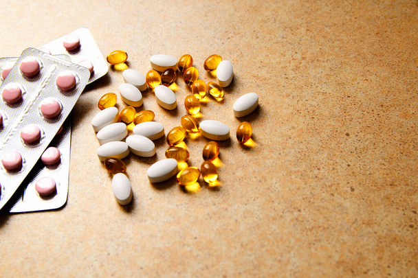 Blister mit rosa Tabletten und Vitamin D und Kapseln mit Fischöl liegen chaotisch vor dem Hintergrund einer Sandarbeitsplatte - Foto, Bild