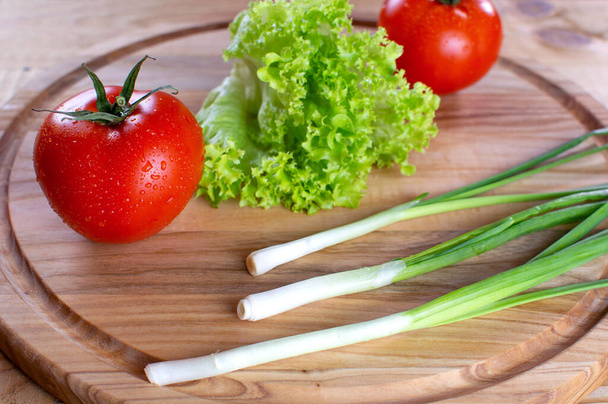 Saftige rote Tomaten, auf einem hölzernen Hintergrund, mit Salat und Schnittlauch. Vegetarisches Essen. Reife Tomaten, mit Tropfen Wasser. - Foto, Bild